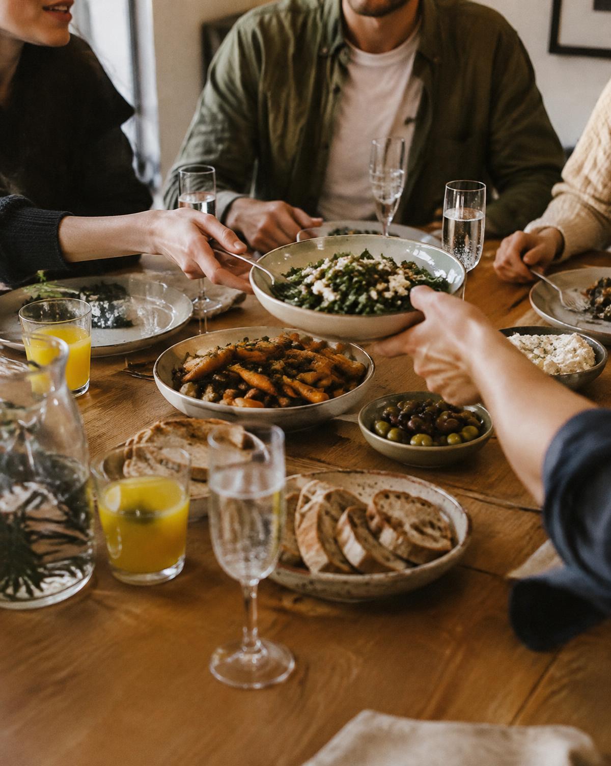 Friends passing plates around a shared dinner table with glasses of sparkling water and juice