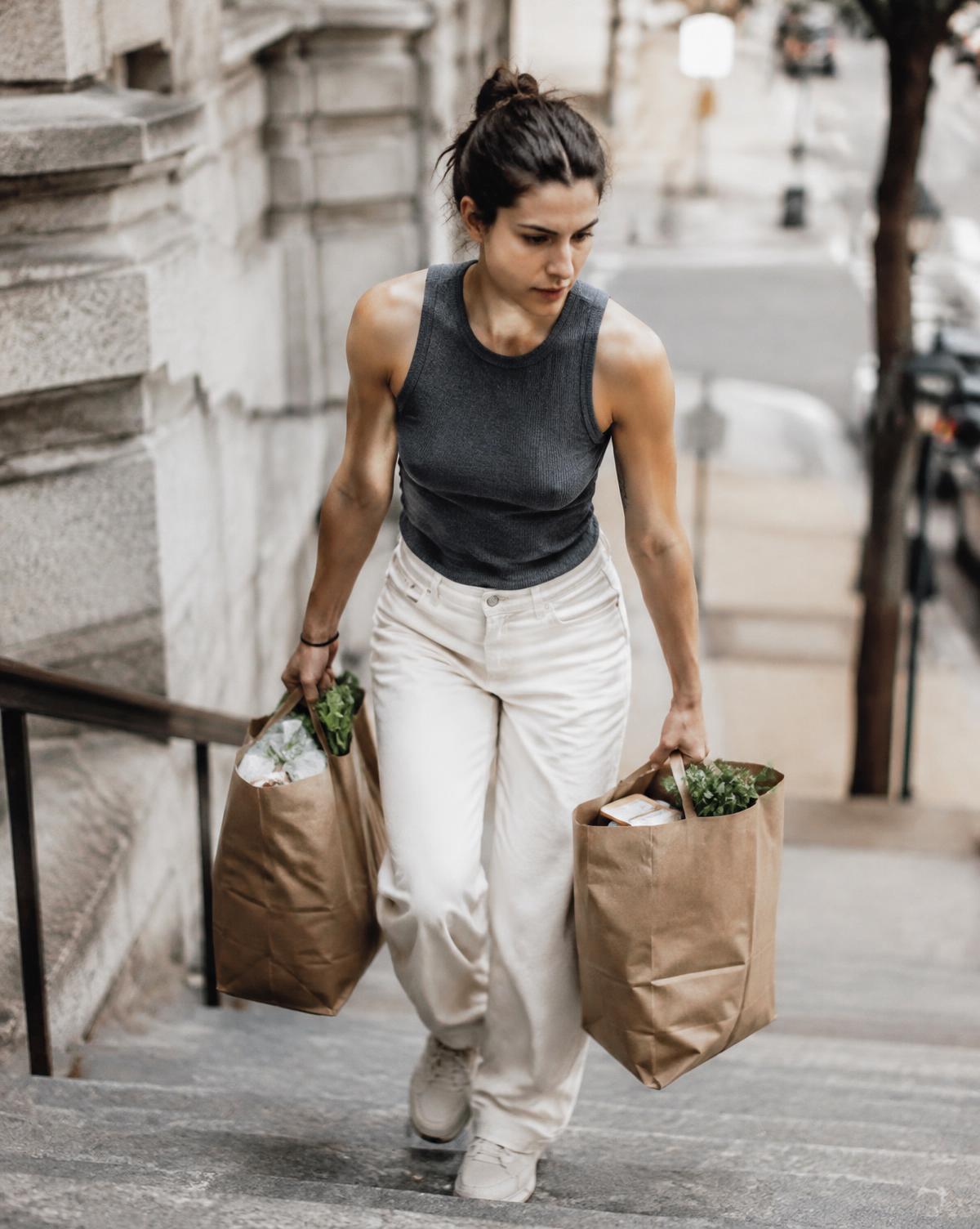 A woman carrying two full grocery bags up stone steps