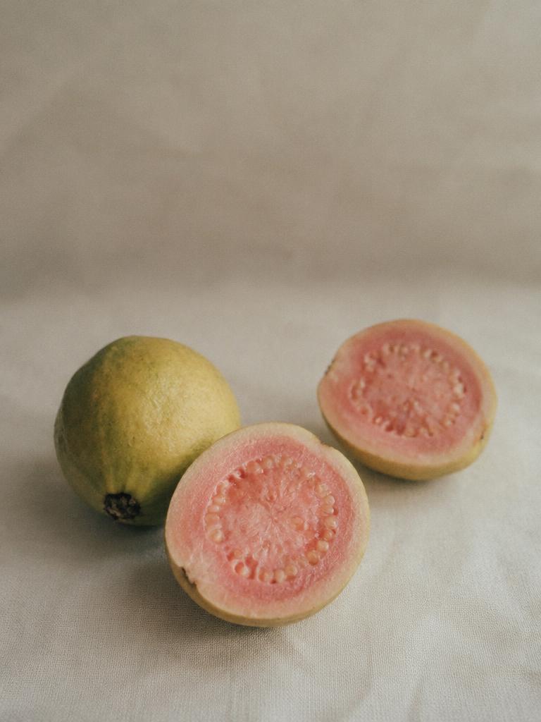 Generated illustrative placeholder: Whole and halved pink guavas on linen